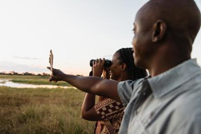 Close up of a guide pointing, with a guest using binoculars beside them.