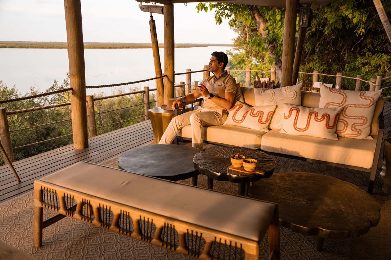 Stunning waterfront luxury safari lodge main area at Wilderness DumaTau, overlooking Osprey Lagoon in the Linyanti Wildlife Reserve, Botswana. The spacious, contemporary deck features elegant seating and a plunge pool, offering guests an unparalleled view of the wilderness and the famous elephant mega-herds.