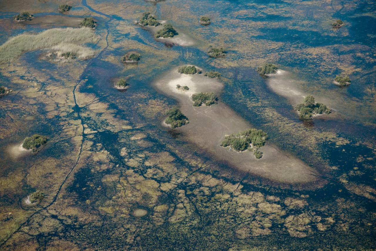 Wide aerial view of the Okavango Delta mosaic of shallow blue water and small bushy islands, illustrating the unique floodplain ecosystem.