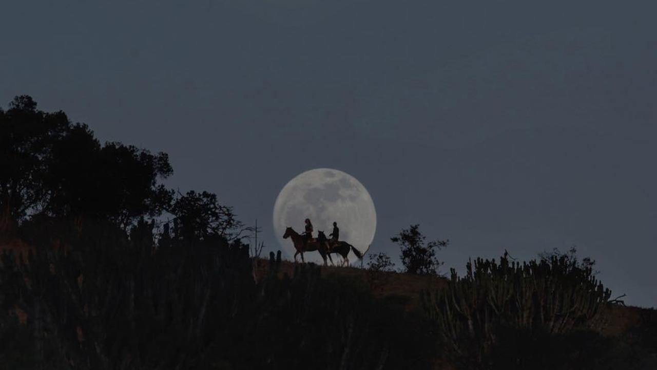 Shot of the full moon with silhouettes of people on horses