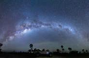 A safari vehicle with tourists parked under a brilliant, sweeping arc of the Milky Way galaxy during a star-gazing safari night drive in Botswana.