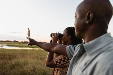 Close up of a guide pointing, with a guest using binoculars beside them.