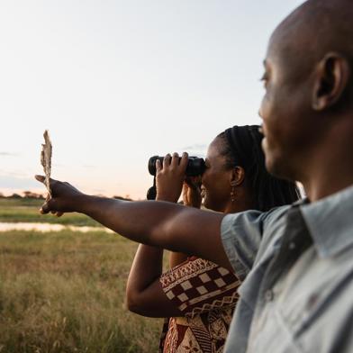 Close up of a guide pointing, with a guest using binoculars beside them.