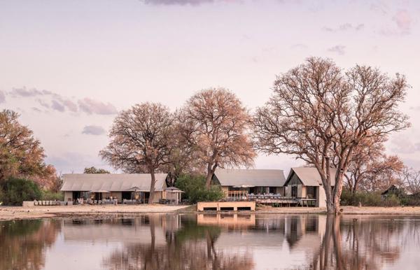 A tented camp in the background, and a waterhole in the foreground.