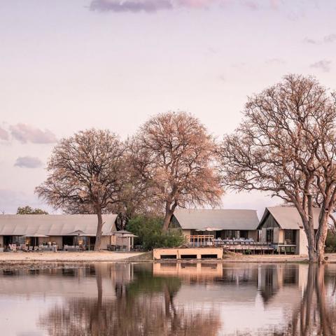 A tented camp in the background, and a waterhole in the foreground.