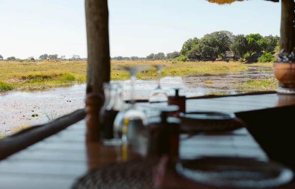 A beautifully set table on a wooden deck overlooks a tranquil body of water at sunset