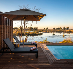 View of pool loungers and an umbrella poolside, with a river in the background